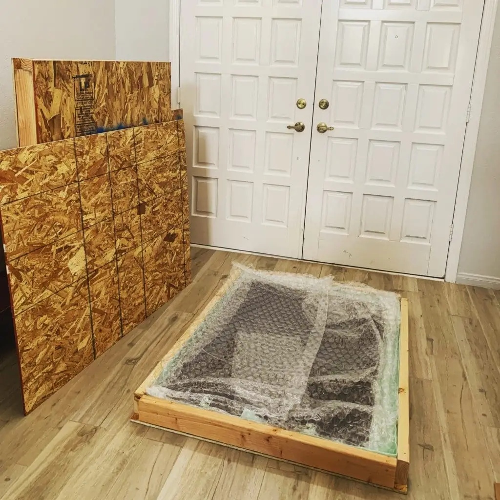 Protected flat item inside an open wooden frame, with packing panels nearby.