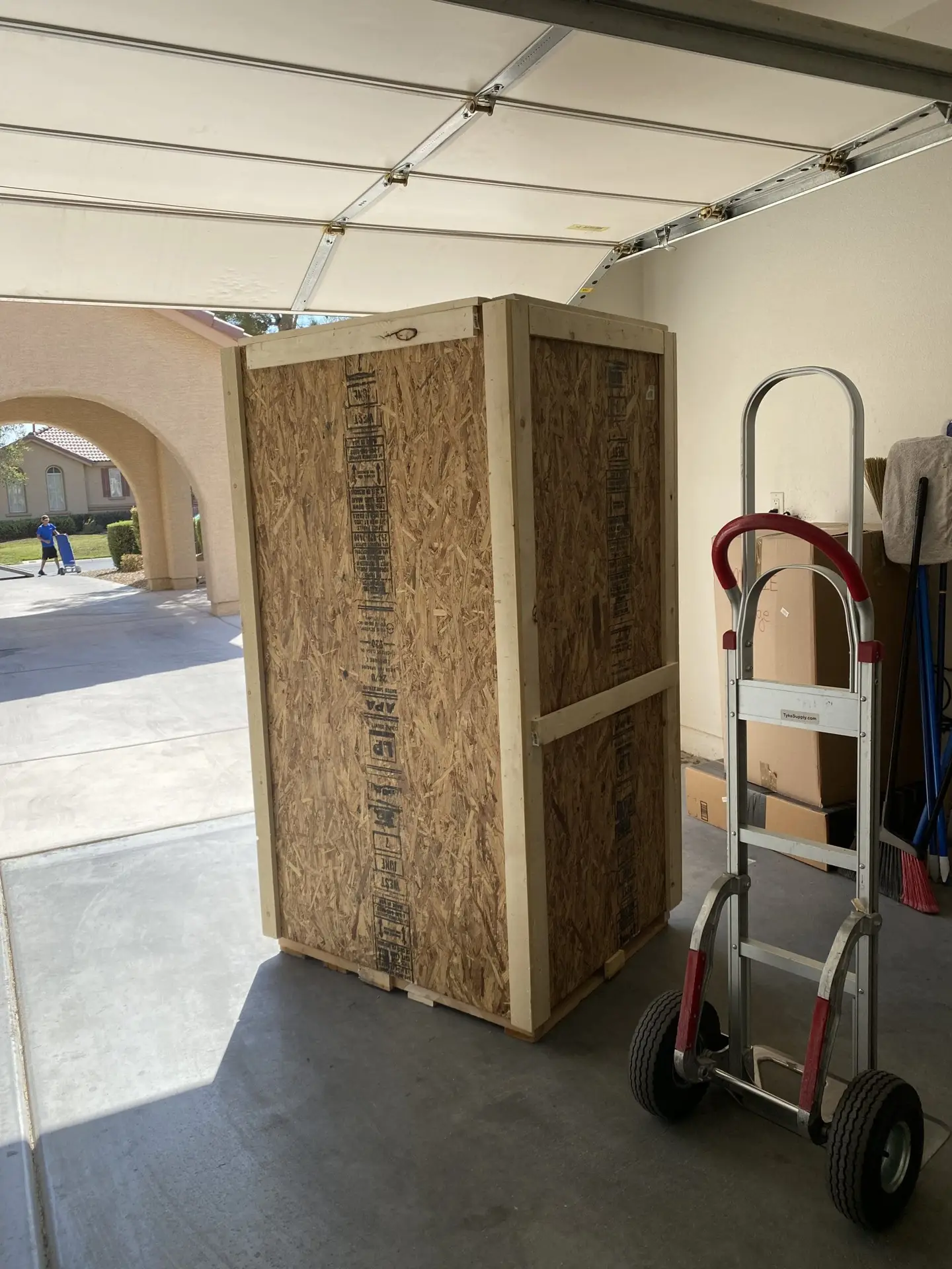 Tall wooden crate with framed panels beside a hand truck in a garage