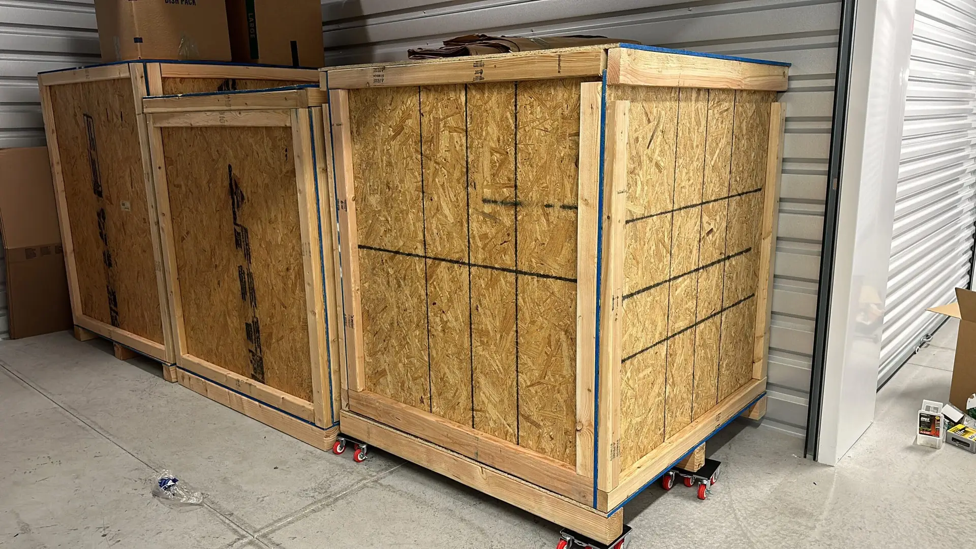 Large framed wooden crate with black straps inside a storage unit