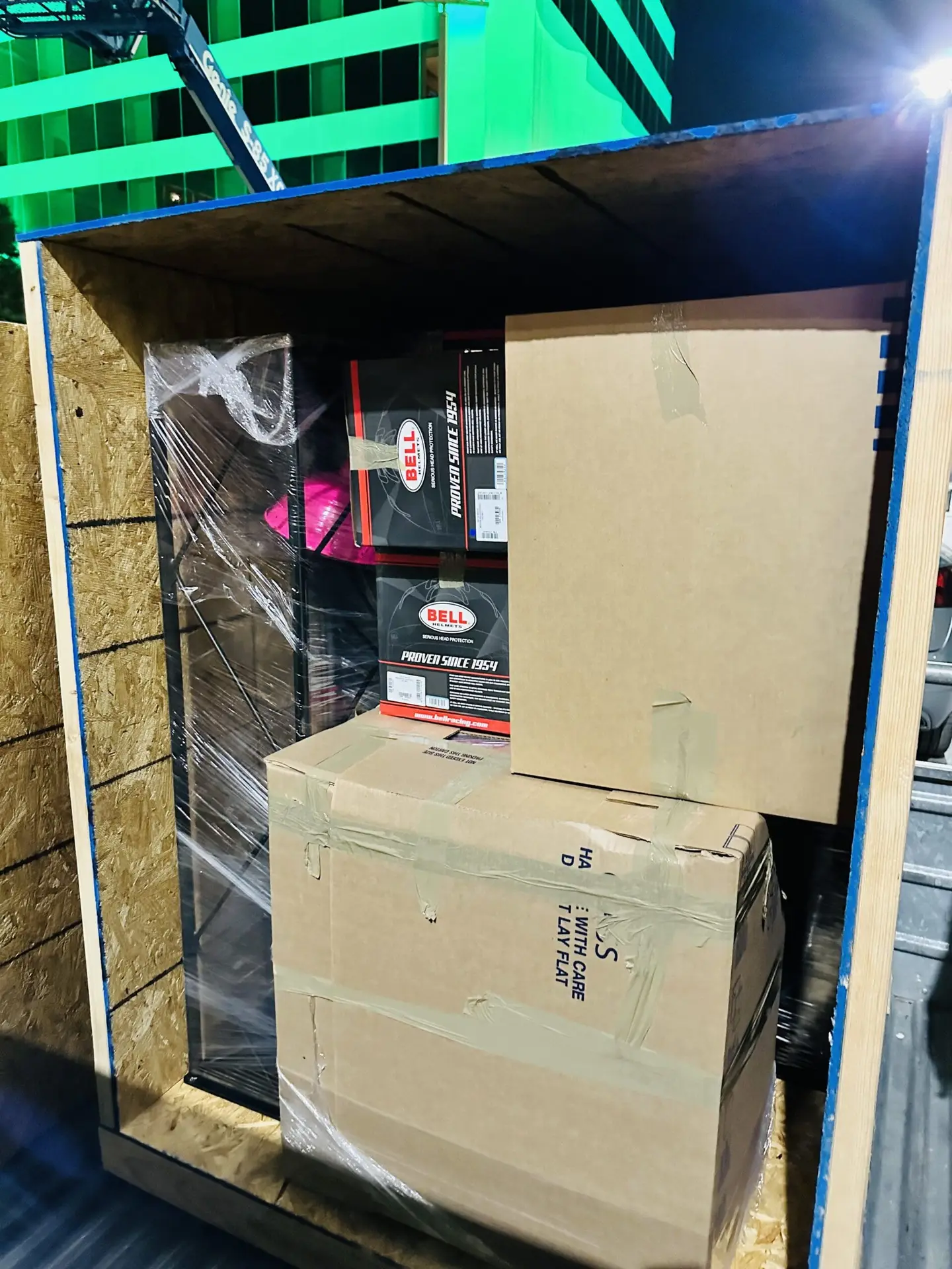 Cardboard cartons and wrapped items inside an open upright wood crate