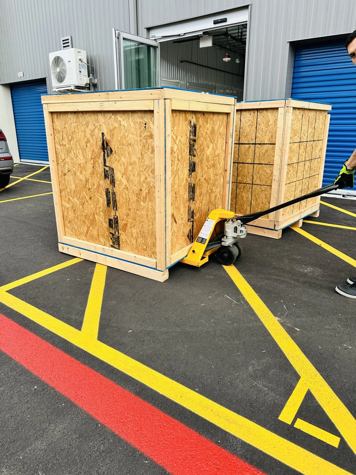 Two wooden shipping crates beside a pallet jack outside a warehouse.