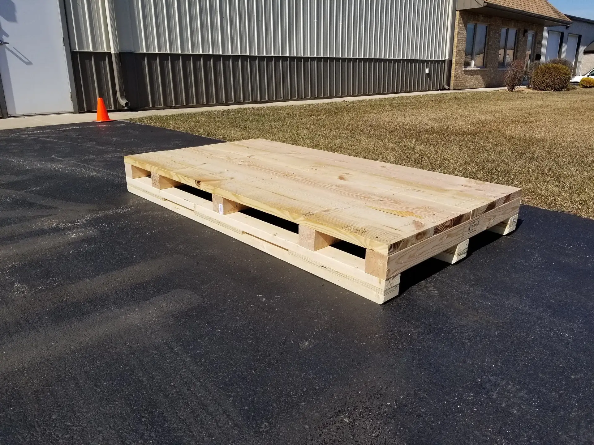 Long wooden pallet on pavement outside a building.