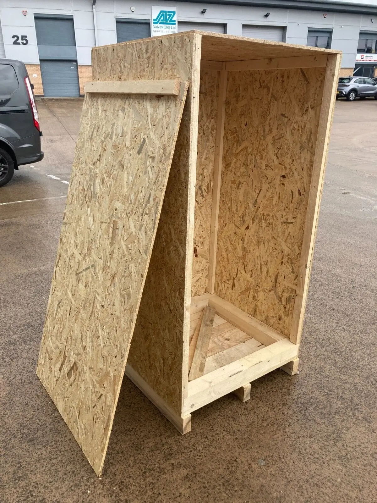 Tall open wooden crate with its removable panel leaning beside it.