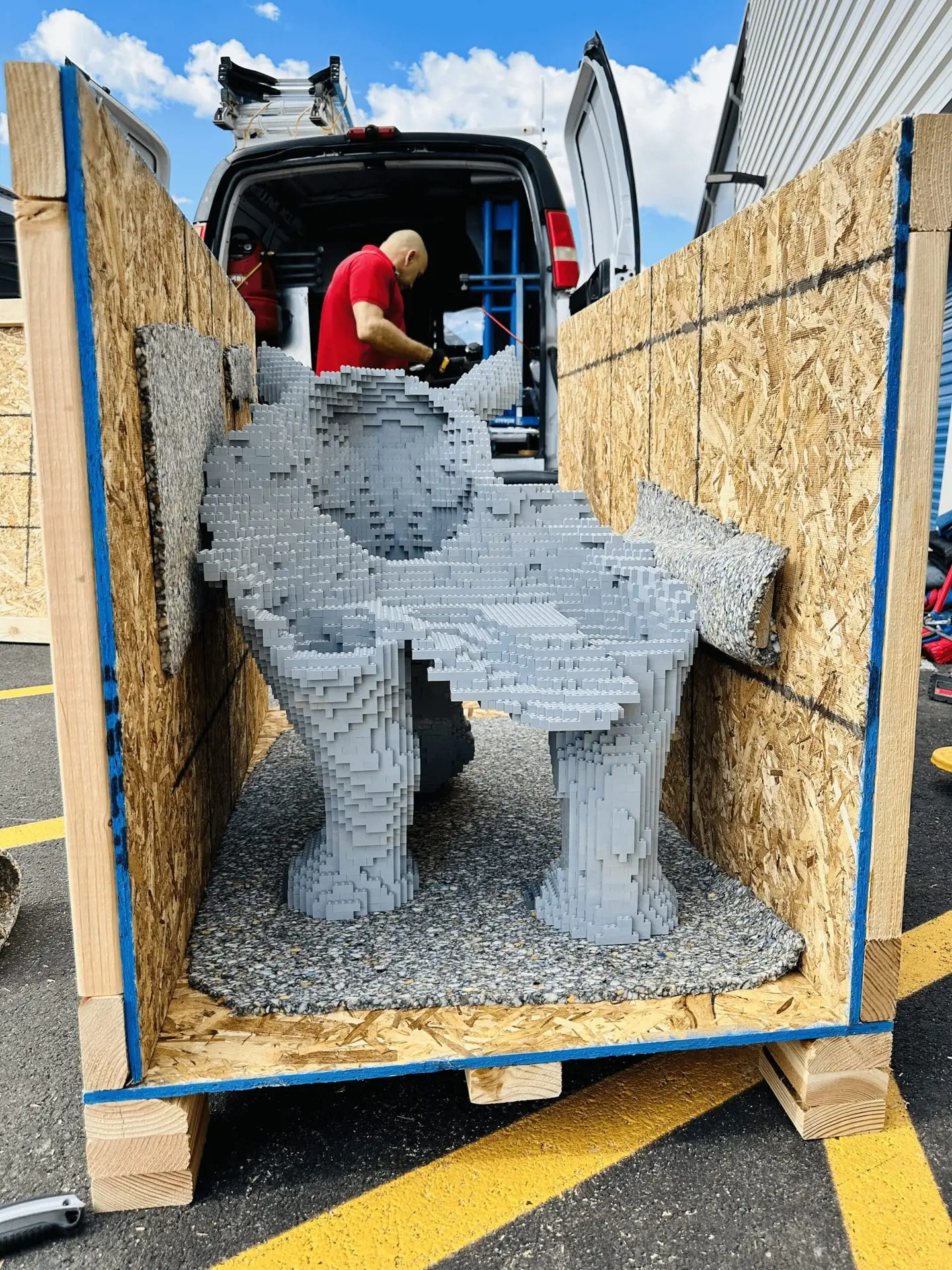 A gray sculptural object supported inside an open wooden crate.