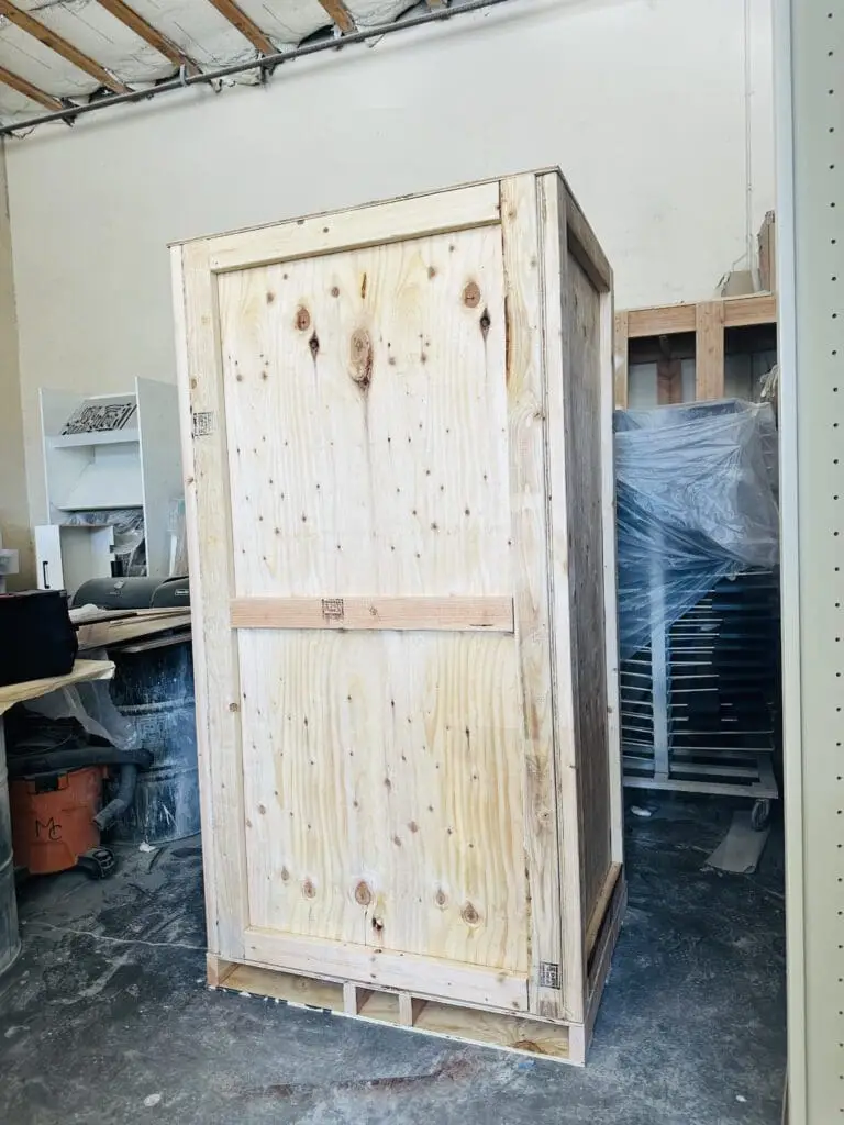 A tall closed plywood crate standing on a workshop floor.