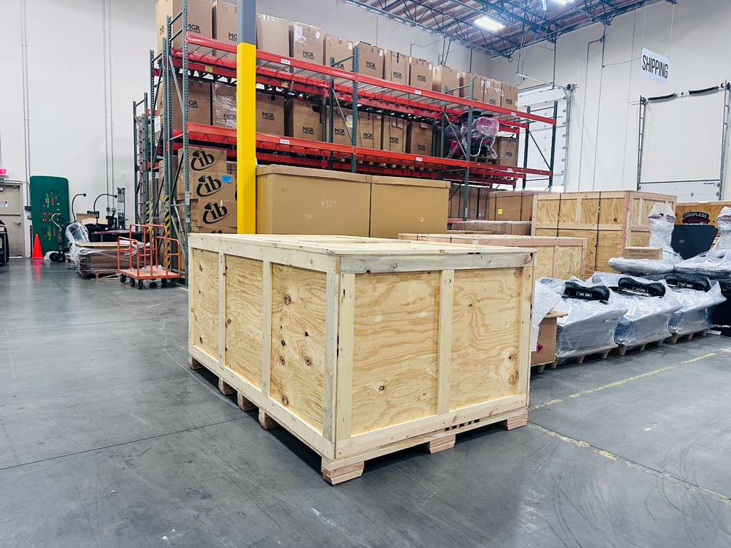 Heavy-duty wooden crate on pallet in industrial warehouse, surrounded by packaged items and shelving, illustrating custom crating solutions for secure shipping.