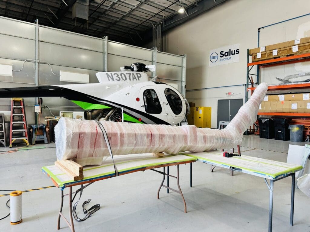 Helicopter rotor blade wrapped for protection on custom pallet in aviation facility, showcasing industrial crating solutions for secure transport.