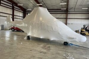 Helicopter heat shrink wrapped for protection during transport, showcasing custom crating services in a spacious warehouse setting.