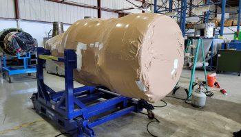 custom shrink wrap solutions Heat-shrink wrapped cylindrical object on a blue crating stand in a packaging facility, illustrating custom packaging solutions for secure transport.